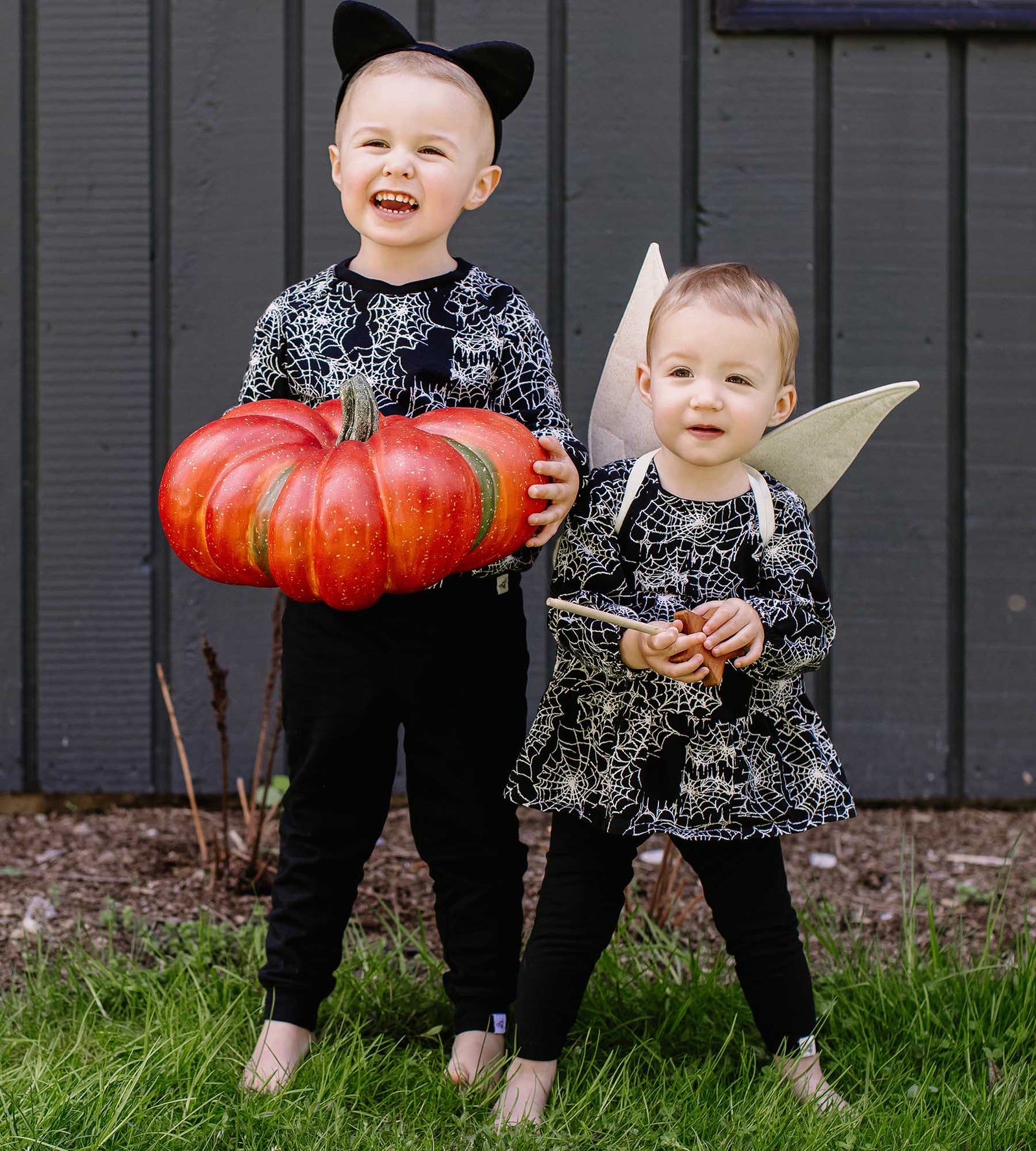 Sibling wearing matching spiderweb print outfits from Burt's Bees Baby holding orange pumpkin
