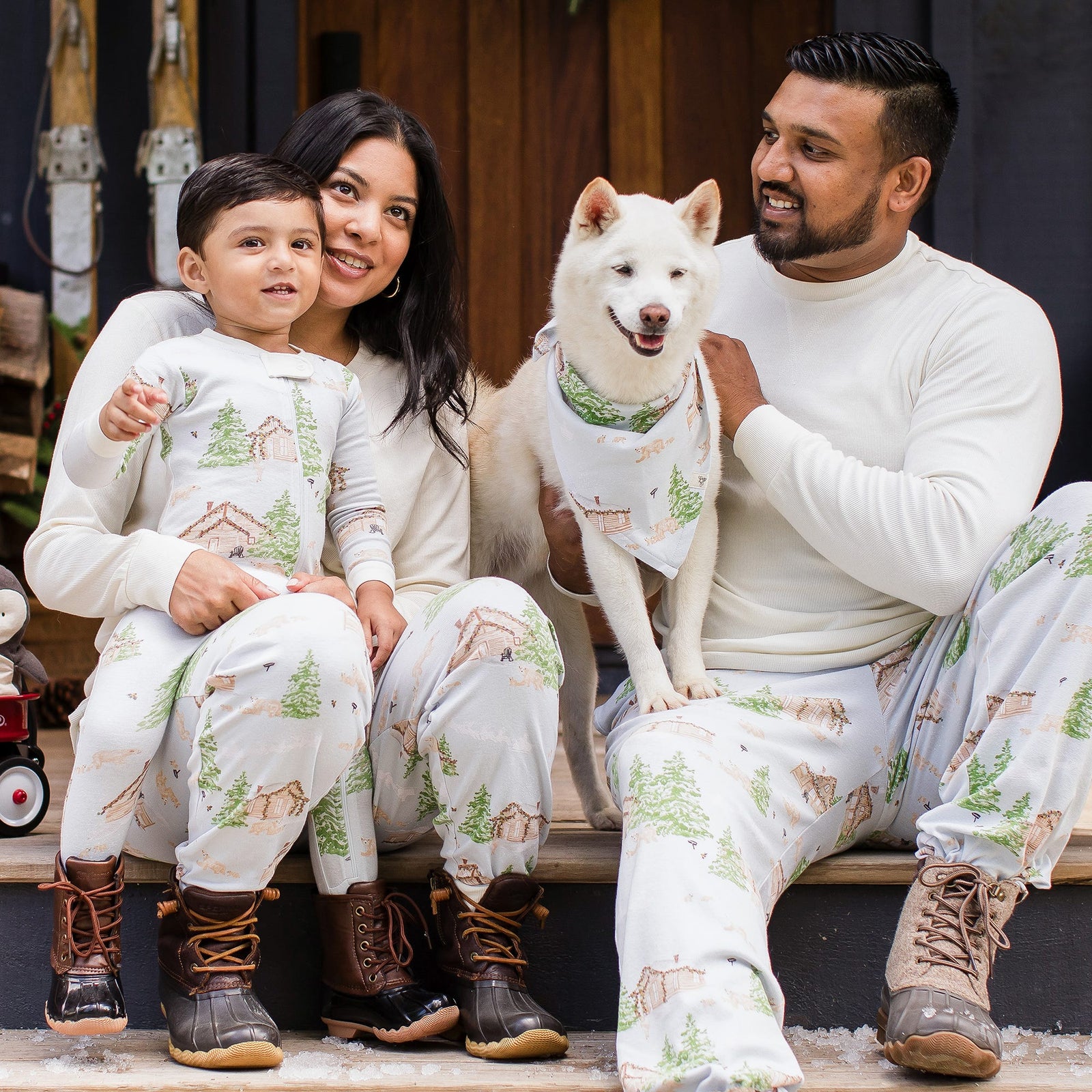 Family sitting outdoors with dog wearing Burt's Bees Baby matching holiday pajamas and snow boots