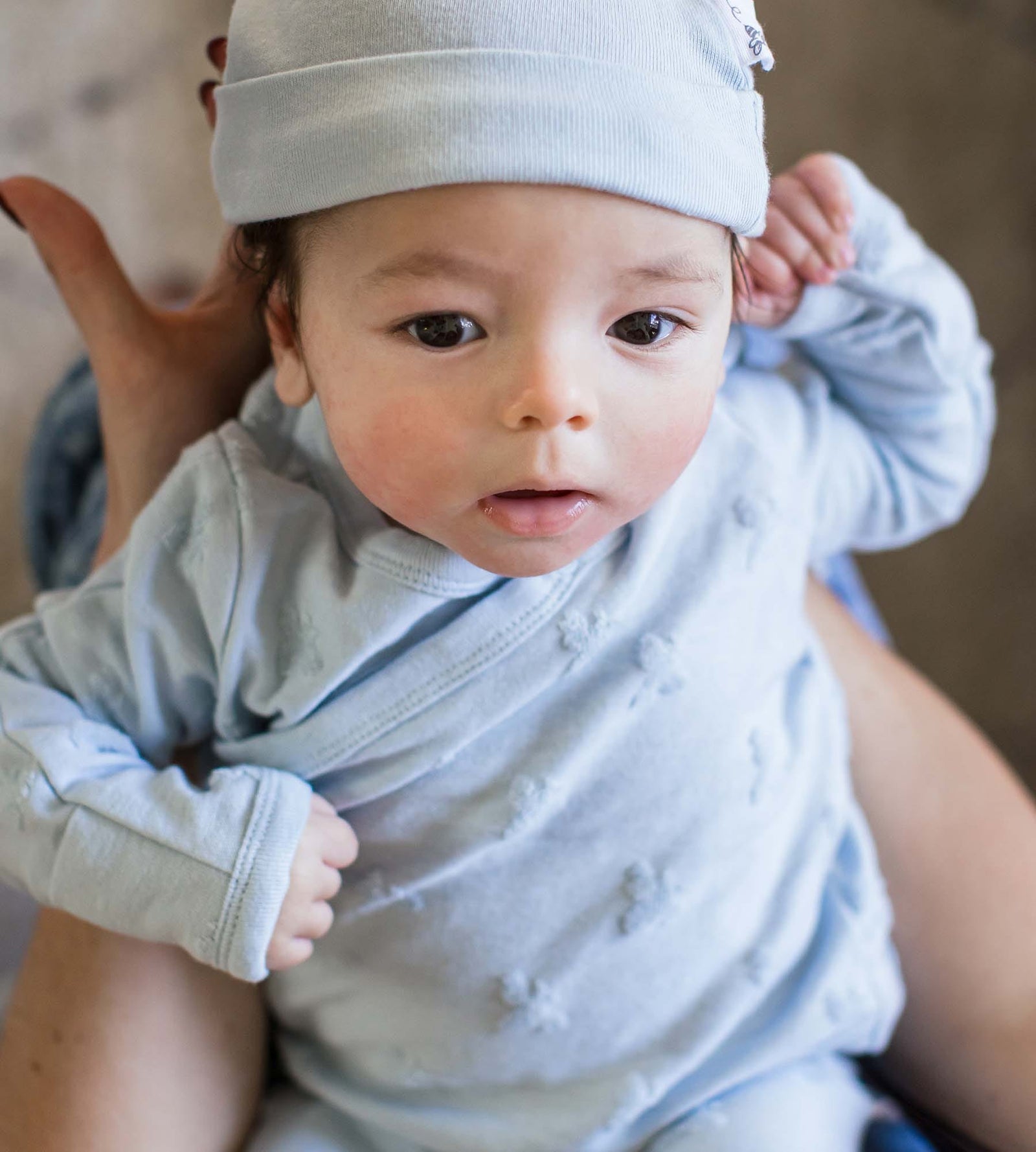 Newborn baby being held by mom wearing blue organic cotton take me home set