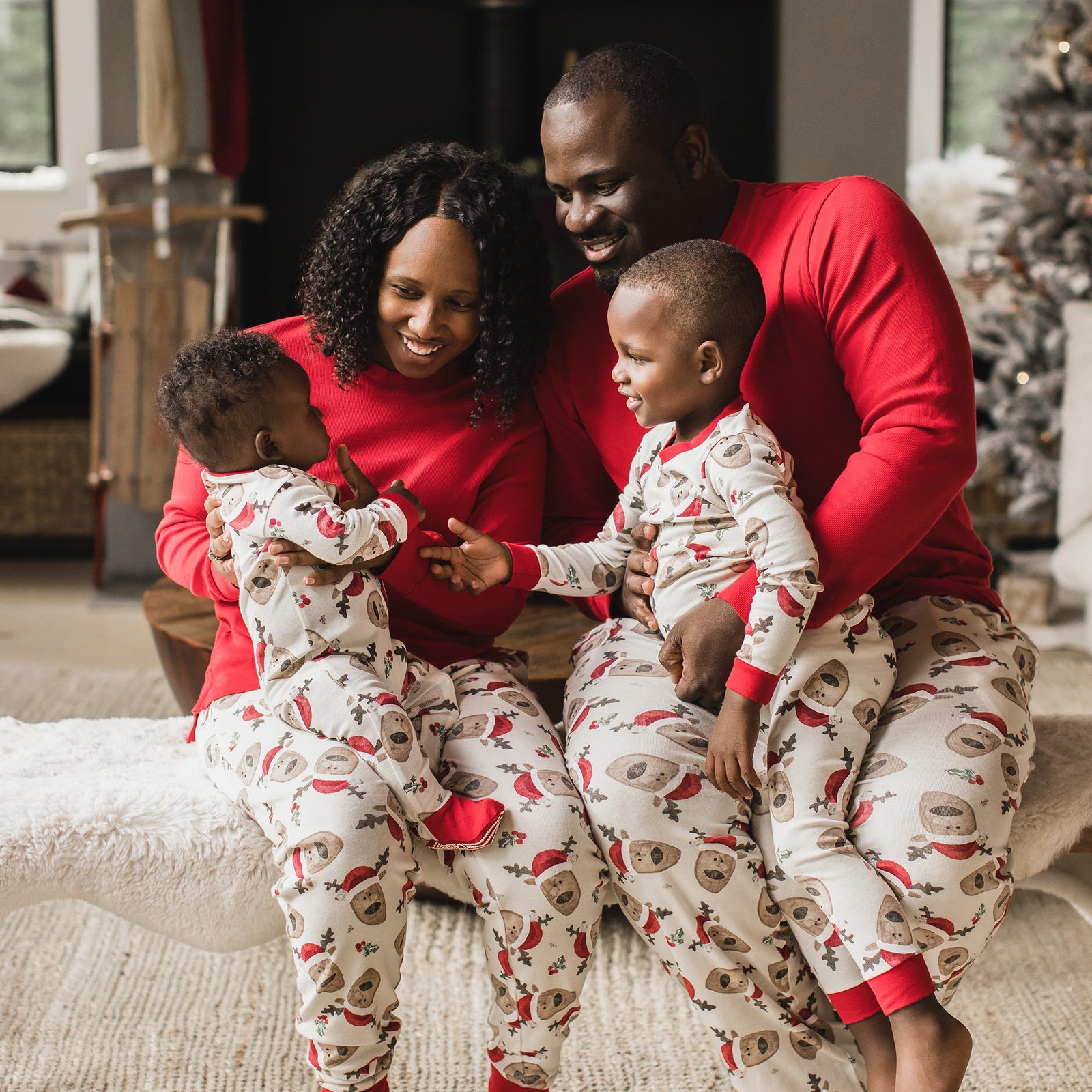 Family sitting on couch with toddler and baby wearing matching reindeer print pajamas from Burt's Bees Baby