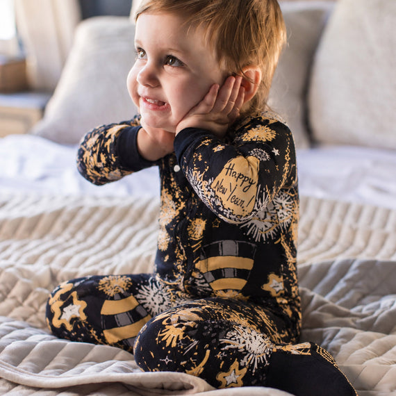 Toddler wearing navy footed sleeper with gold fireworks print, snap front, covered feet