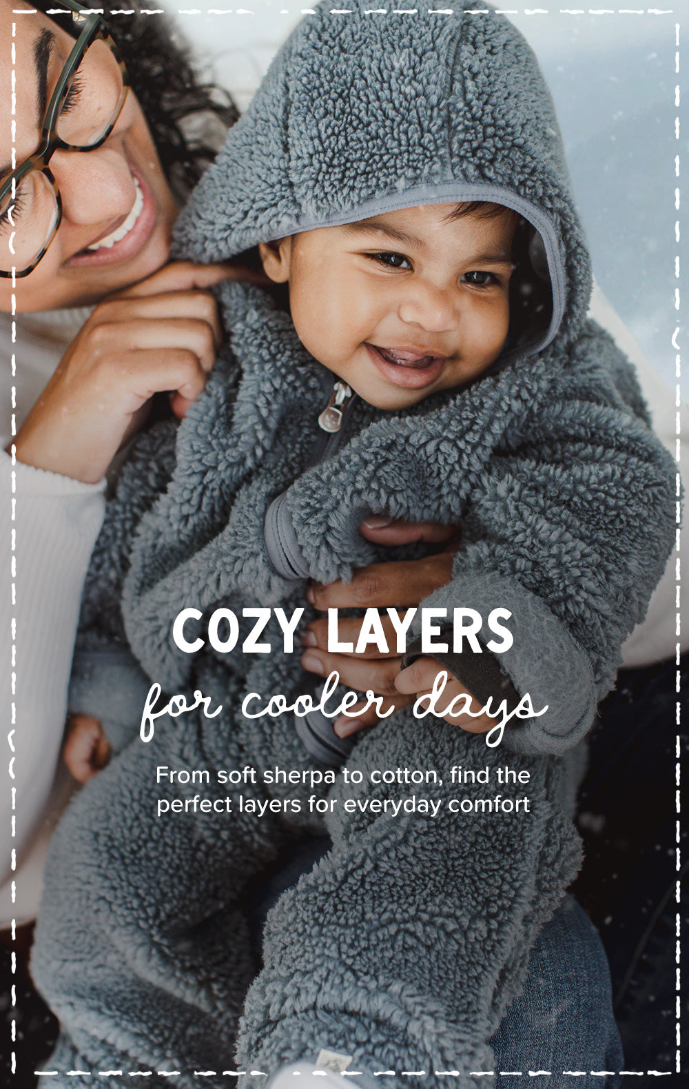 A smiling child wearing a cozy gray sherpa hooded jacket, held by an adult, with overlaid text reading 'COZY LAYERS for cooler days' and a white dashed border around the photo.