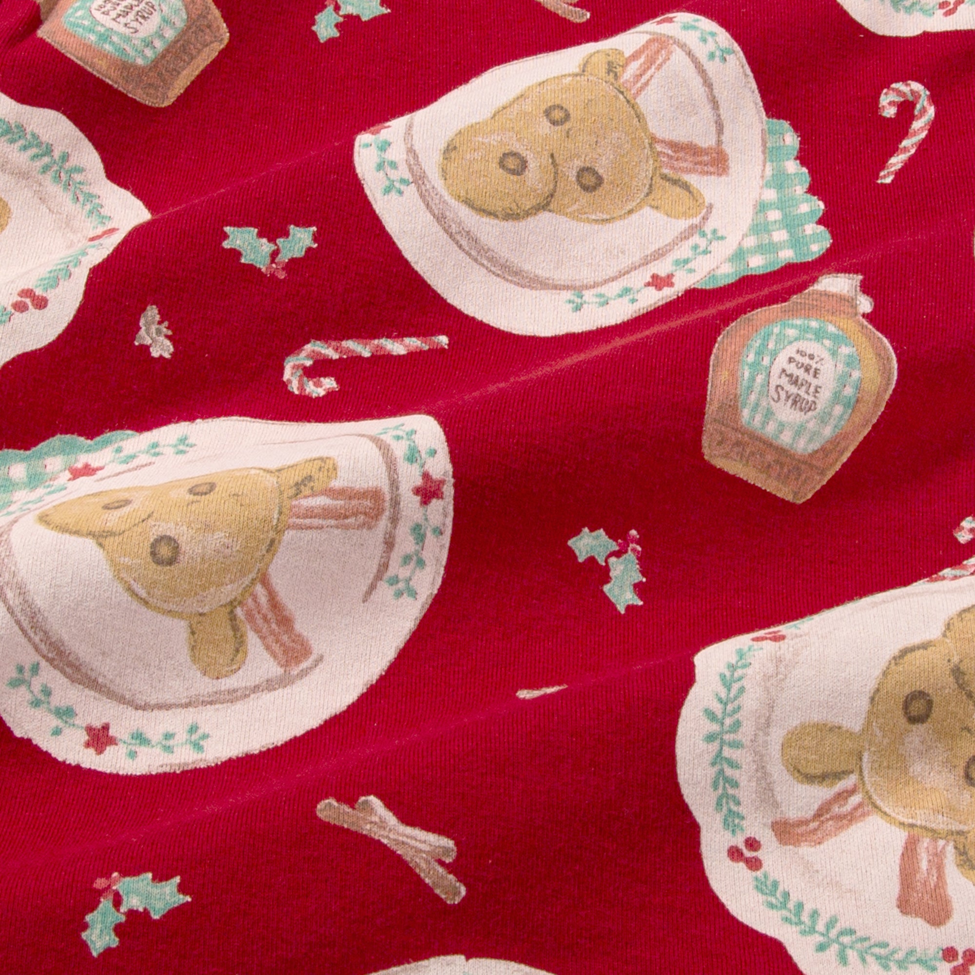Close-up of red pajama fabric with stitched bear-face and small holiday icon print
