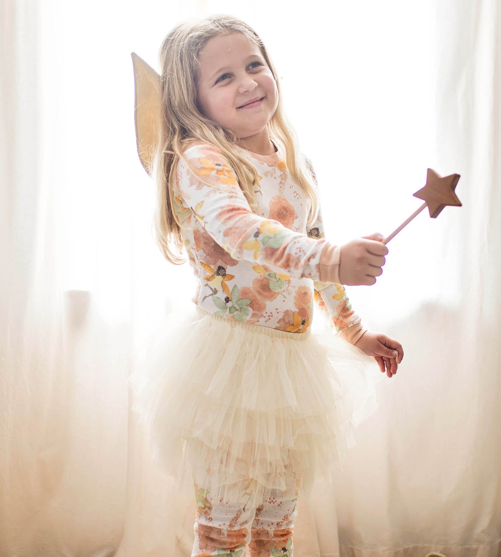 Toddler girl wearing fairy wings and skirt wearing matching watercolor print pajamas with star wand