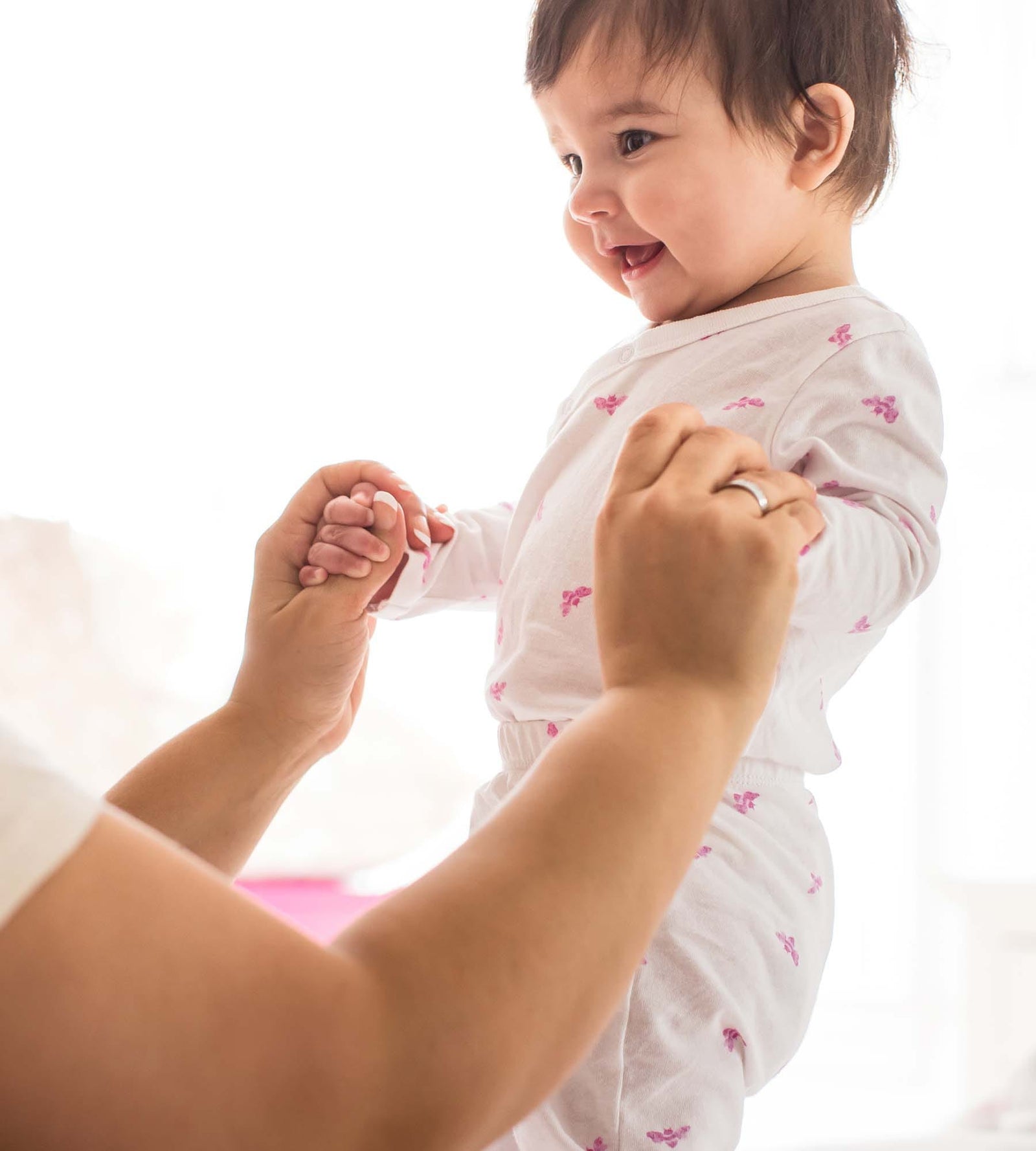 Smiling baby standing holding mom's hands wearing Burt's Bees wrap front pink jumpsuit