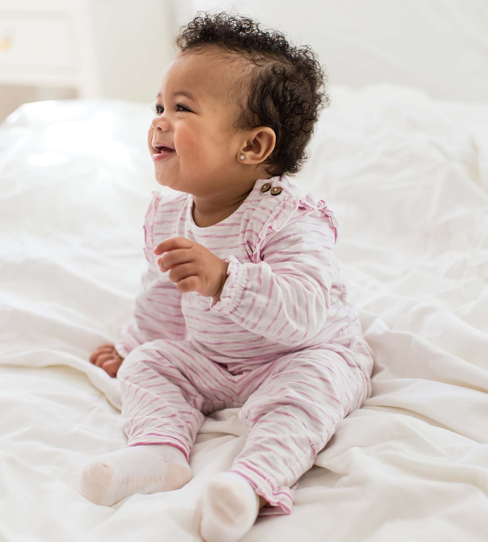 Baby girl sitting on bed wearing organic cotton Slub Stripe Bodysuit Set