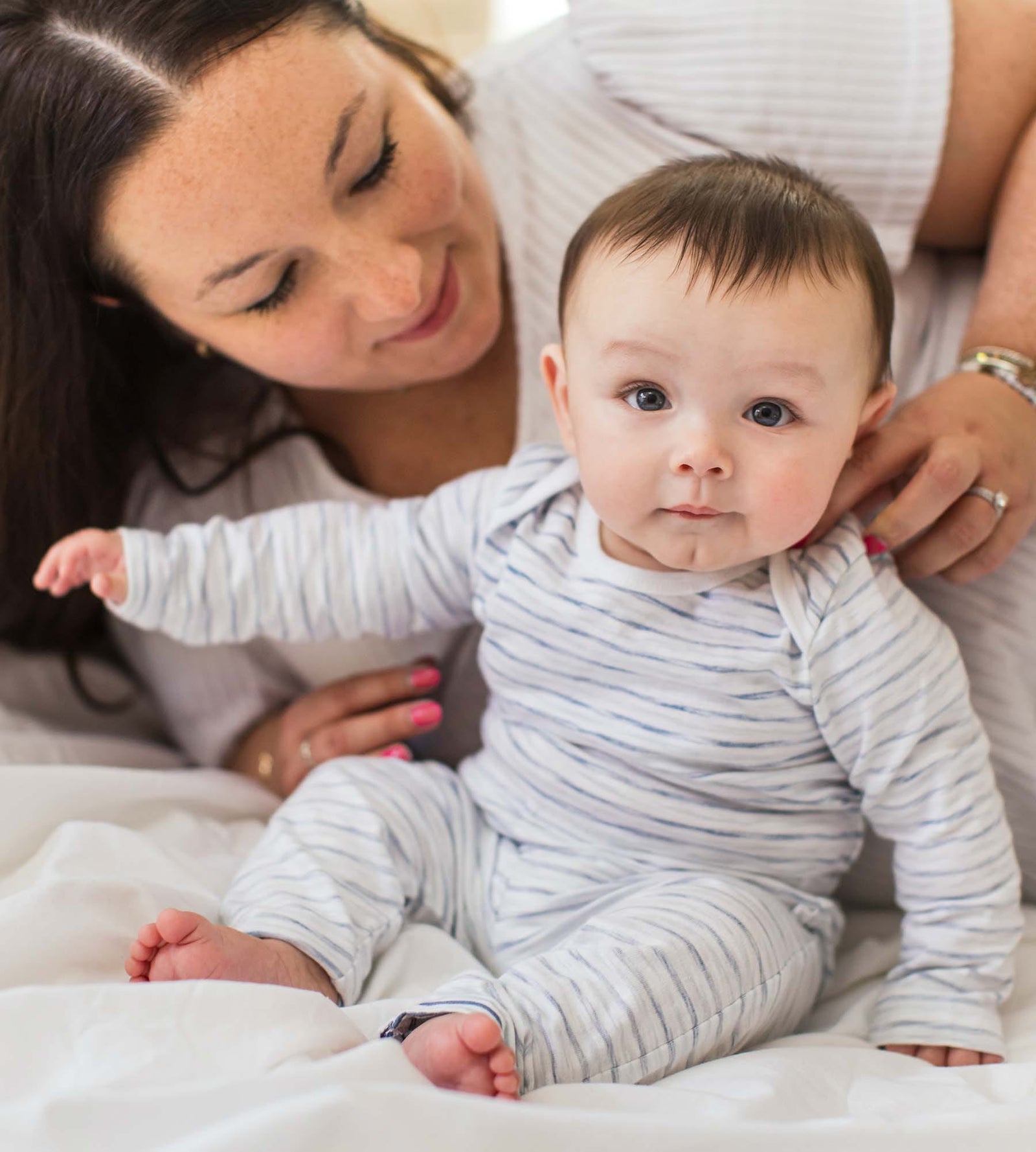 Mom and baby wearing blue stripe organic cotton bodysuit set laying on bed