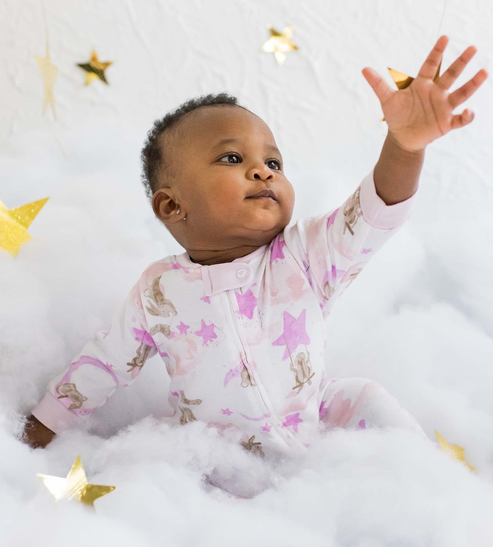 Baby boy sitting and reaching for star props with matching star print organic cotton pajamas