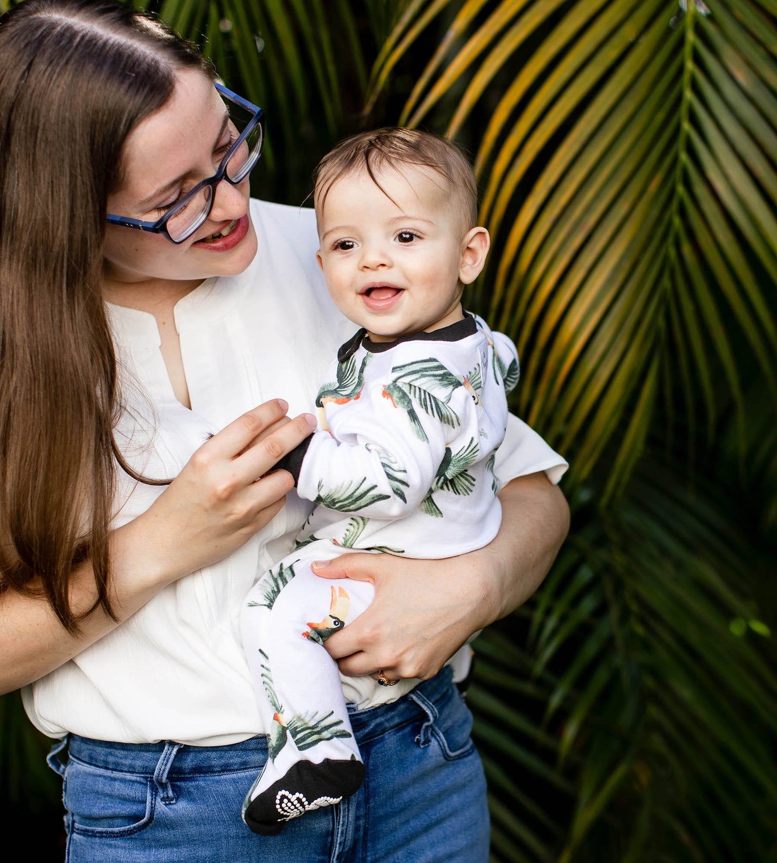 Mom with glasses holding smiling baby wearing tropical toucan watercolor print pajamas