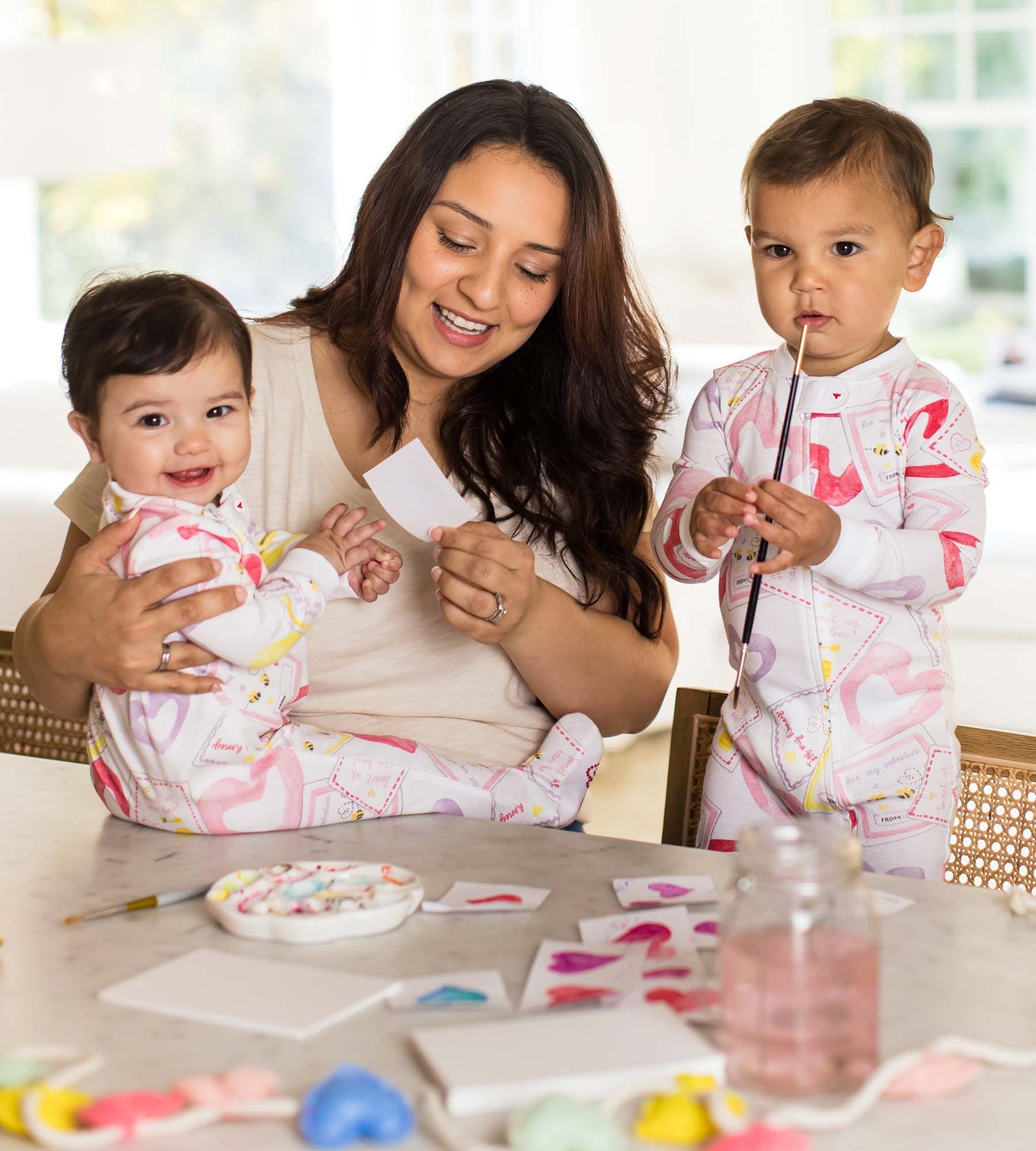 Mom painting Valentine's day cards with two children wearing Burt's Bees Baby Bee Mine print organic cotton pajamas