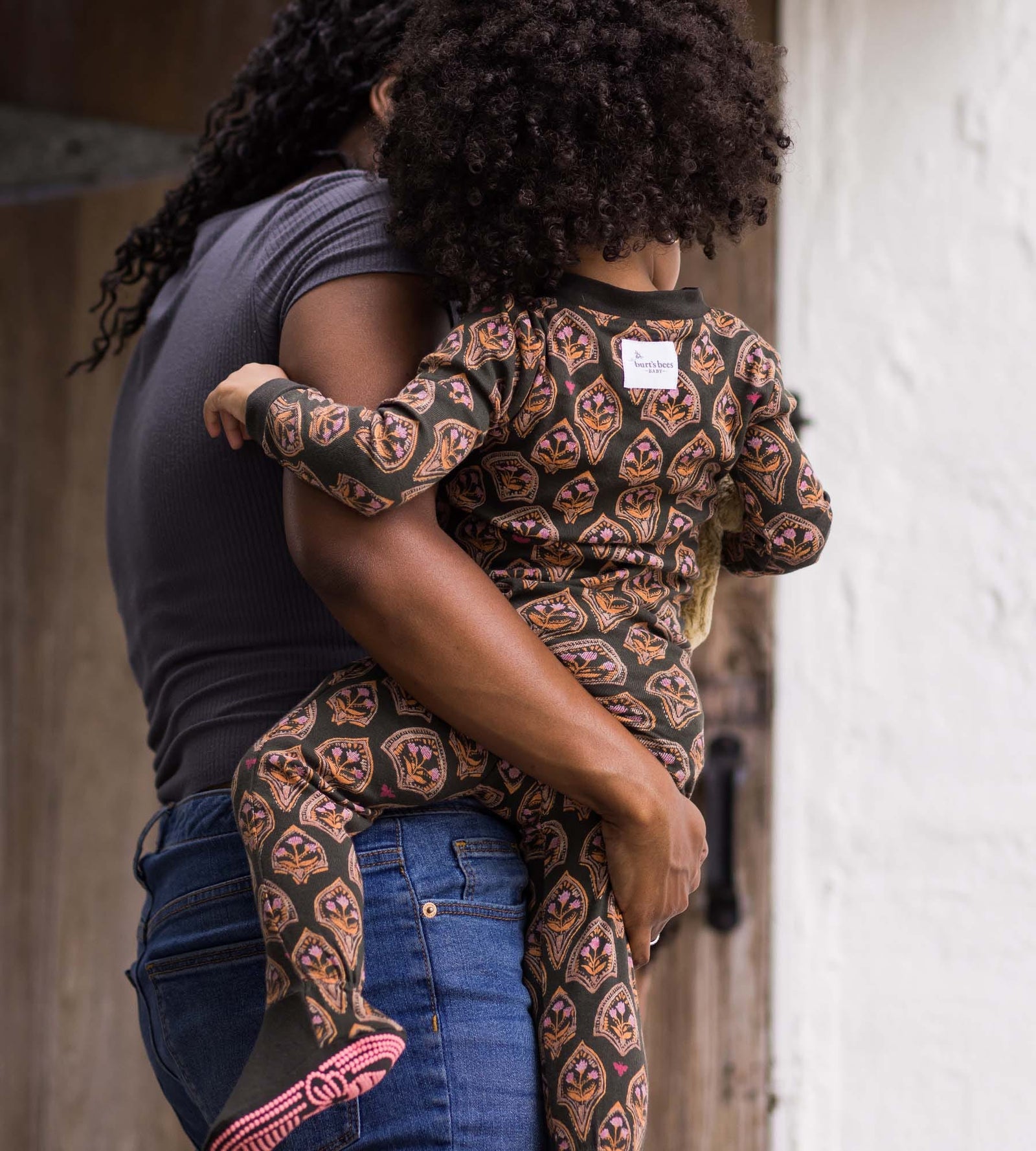 Mom holding toddler girl wearing floral arches print one-piece pajamas from Burt's Bees Baby
