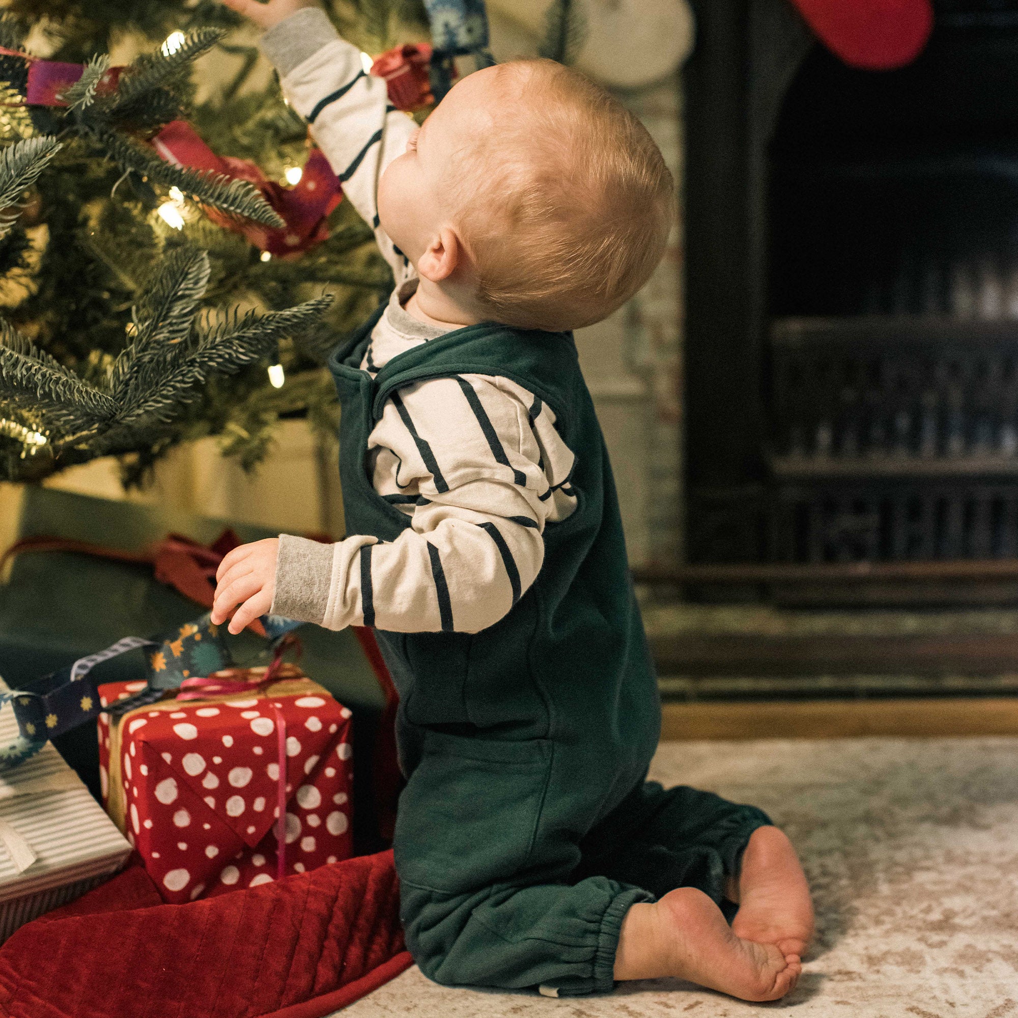 Dark green baby jumpsuit overalls with striped long sleeves, worn while kneeling