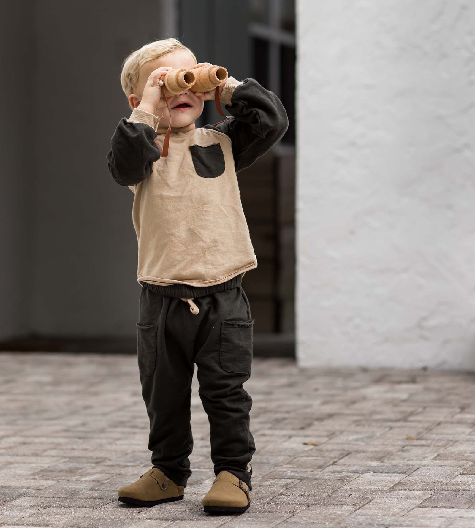 Toddler boy holding binoculars to his eyes wearing organic raglan crewneck set