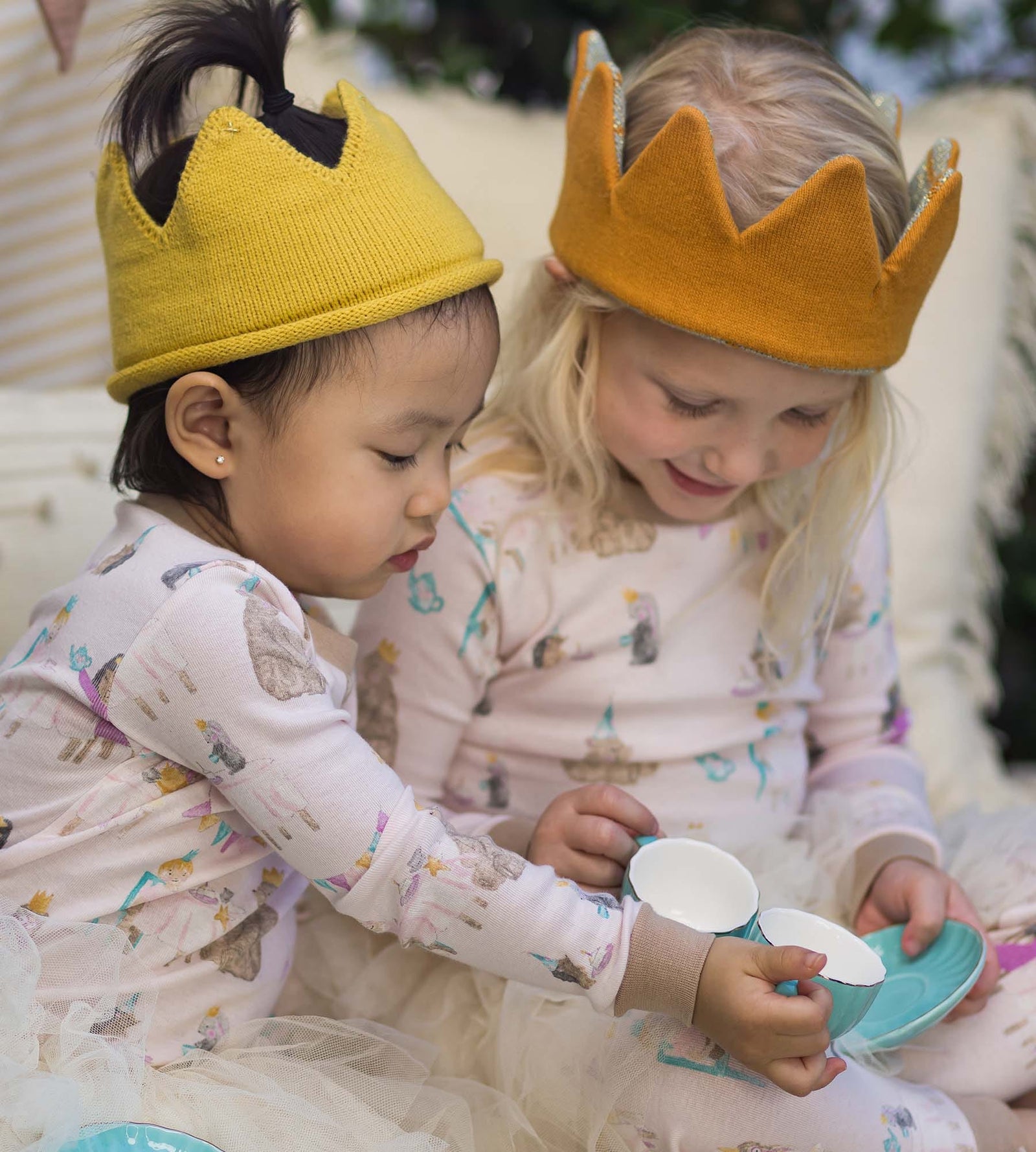 Toddler girls hainge a tea party wearing matching pajamas and cotton crowns