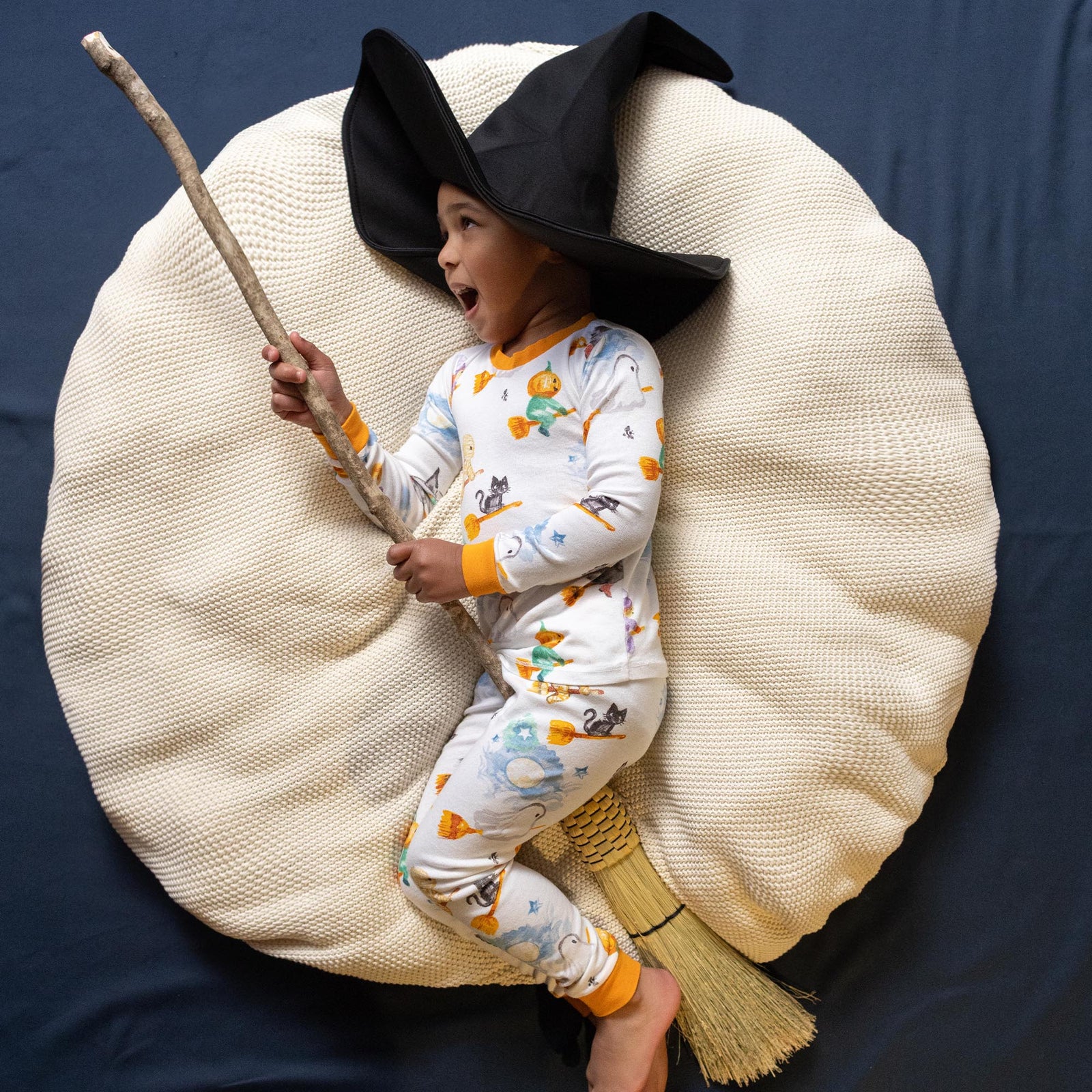 Kids Halloween pajama set in white with orange cuffs, worn with a large black hat - View 2