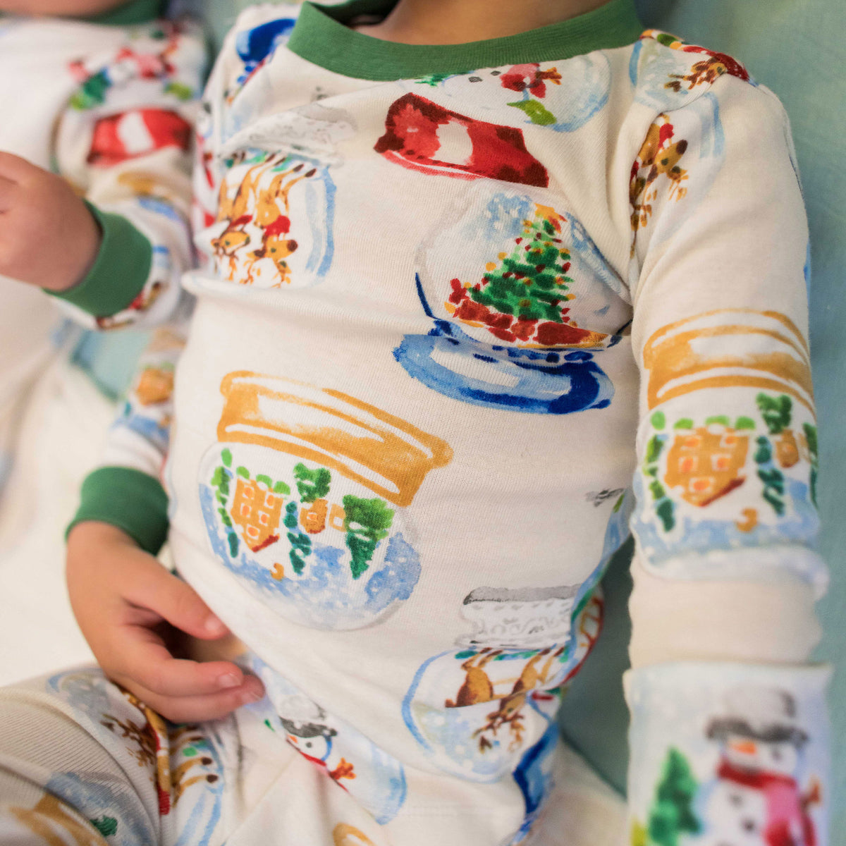 Footed organic cotton baby sleeper with long sleeves, green cuffs, and colorful snowglobe scenes - View 2