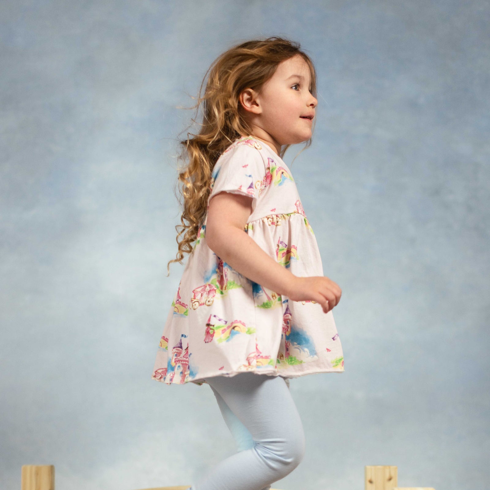 Girl wearing a white princess-themed tunic with blue leggings, side view - View 2