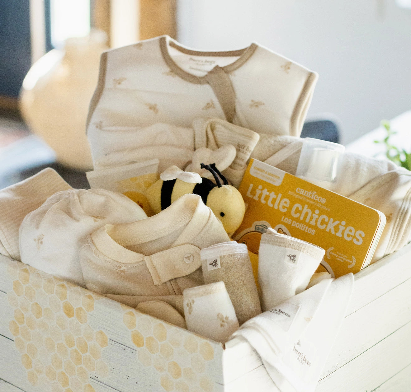 Gift box filled with Burt's Bees Baby clothing and baby essentials displayed in a bright, naturally lit room during the daytime.