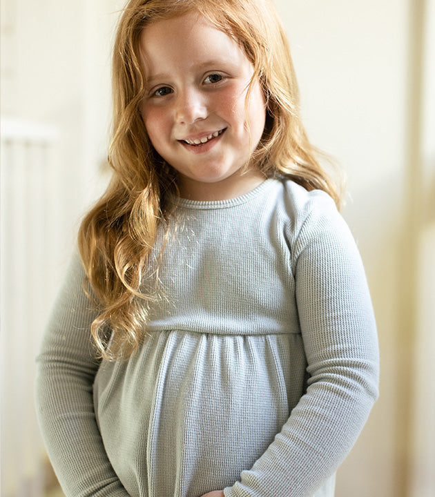 Young girl wearing snowflake flurries organic tunic & pants set, a light gray tunic with long sleeves against a neutral background